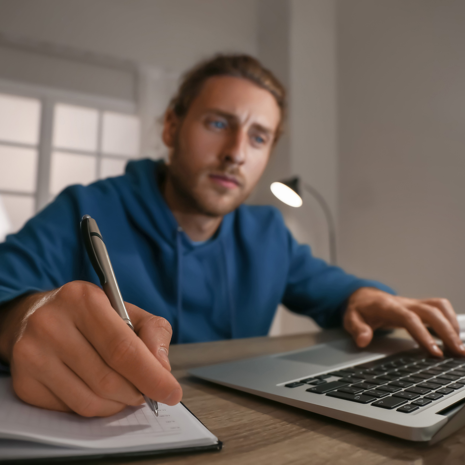 Homme prenant des notes face à un ordinateur portable